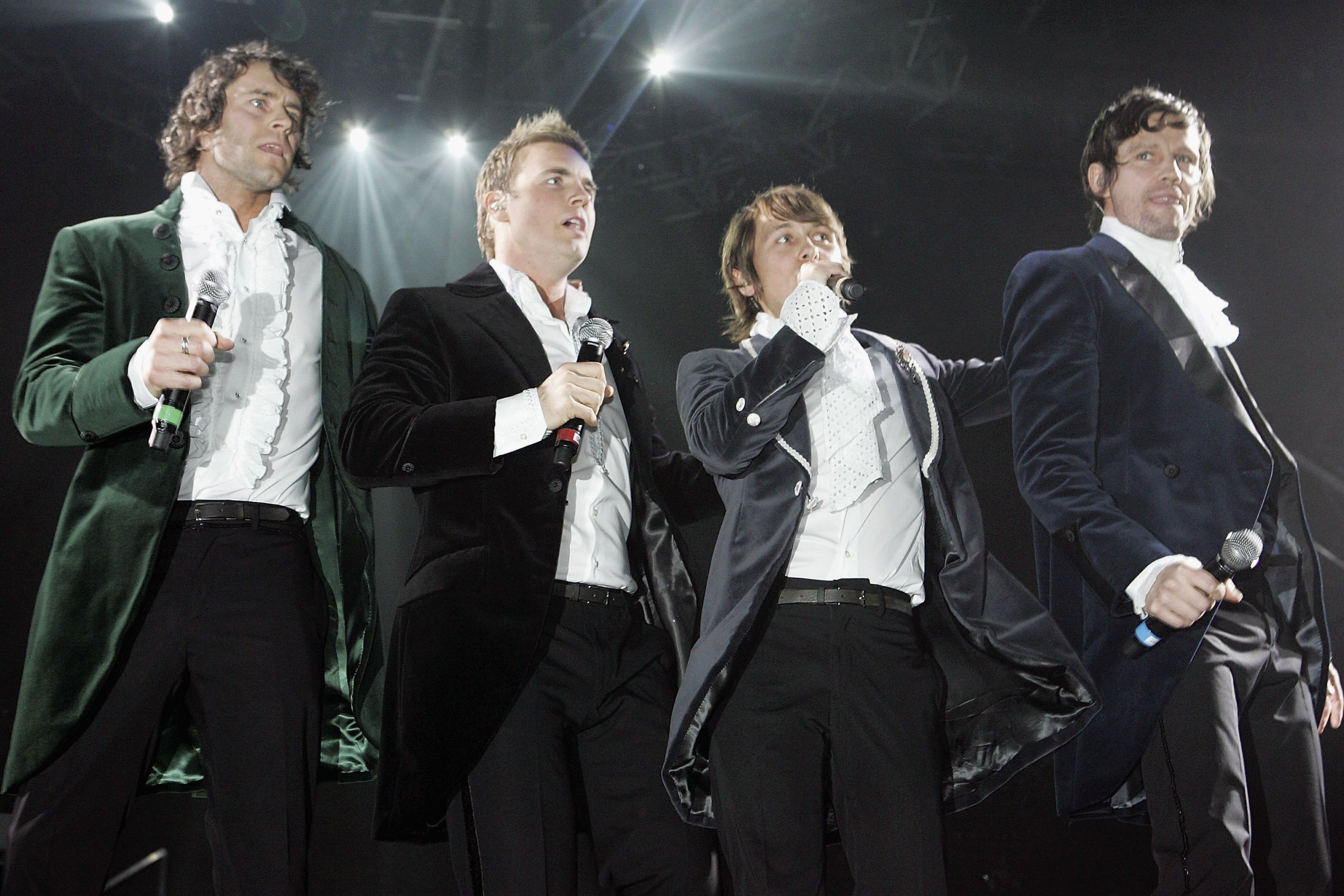 Four members of Take That perform on stage in black suits in 2006