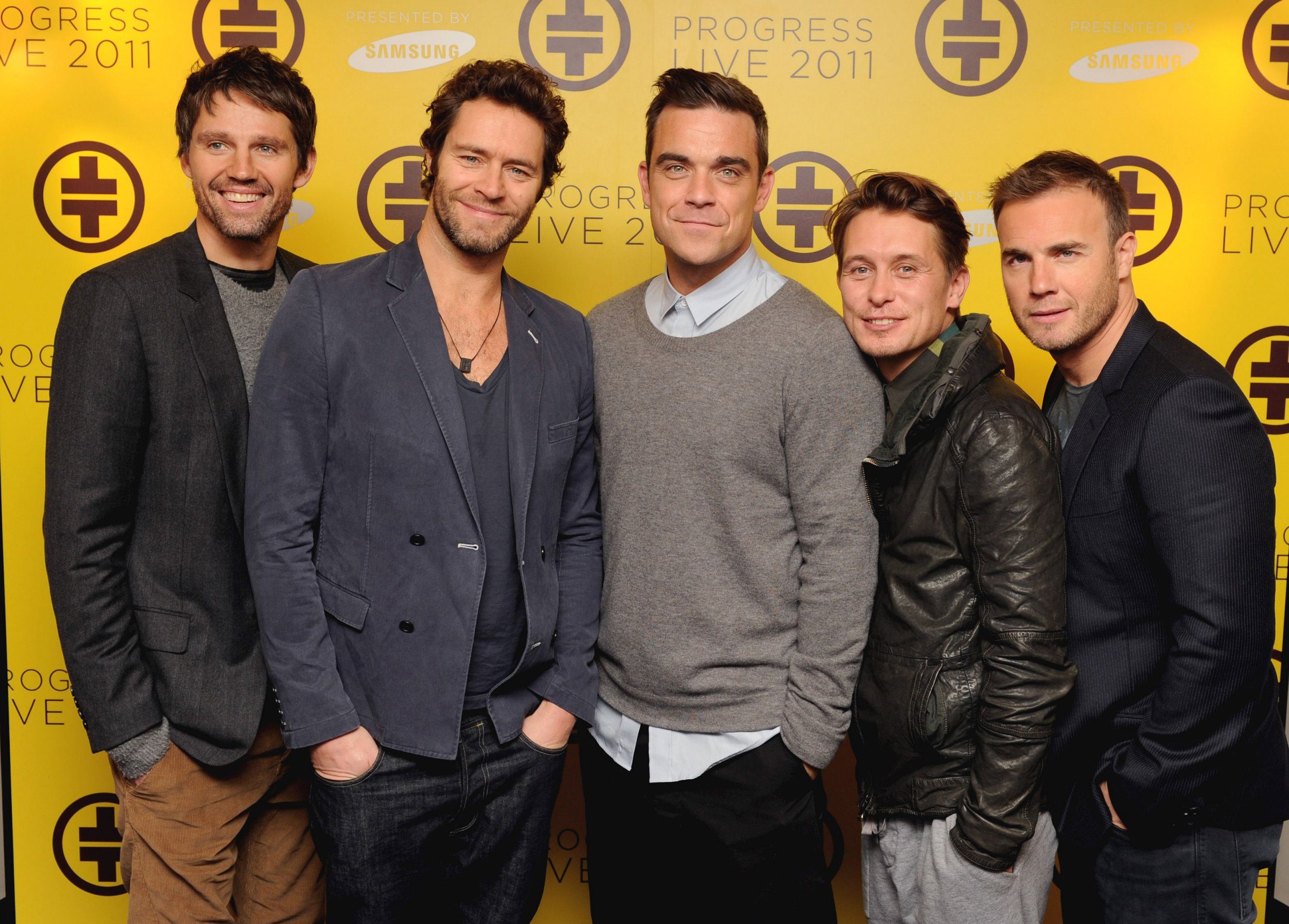 Members of Take That pose for a photo against a yellow background